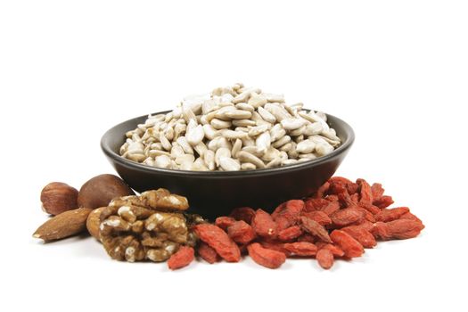 Sunflower seeds in a black bowl with mixed nuts and goji berries on a reflective white background