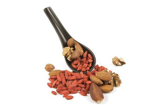 Red dry goji berries with mixed nuts on a small black spoon with a reflective white background