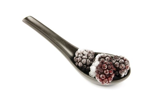 Ripe frozen blackberries on a small black spoon with a reflective white background