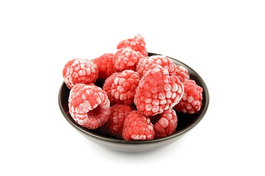 Red ripe frozen raspberries in a small black bowl on a reflective white background