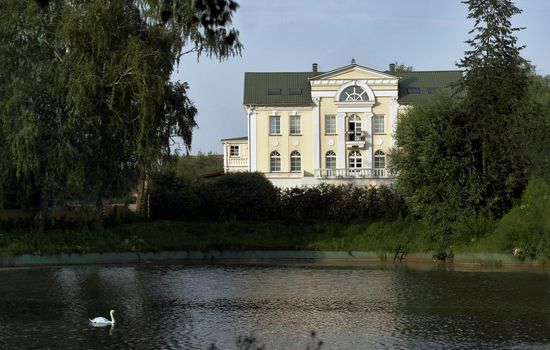 Big house beside pond with white swan. Europe, summer.