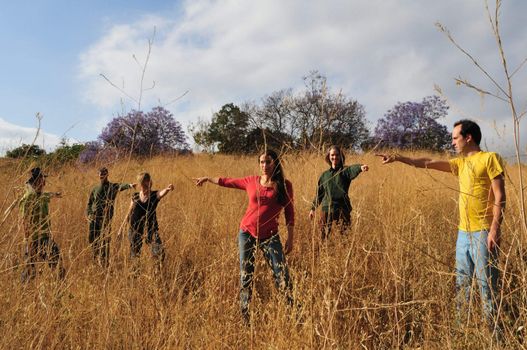 Group of six people pointing in different directions while standing in a field of very tall dried grass