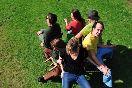 Six friends playing the game musical chairs - two are trying to fit on one chair, and another is falling off his little chair.