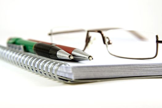 Pen, pencil and glasses on spiral notebook on white background