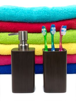 Toothbrushes in toothbrush holder and a lotion dispenser isolated against colored bathroom towels