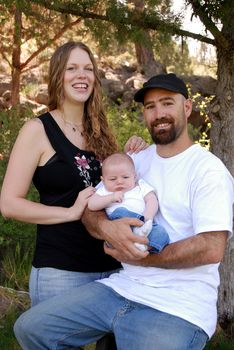 Vertical image of a young modern family with a newborn baby in the park. 