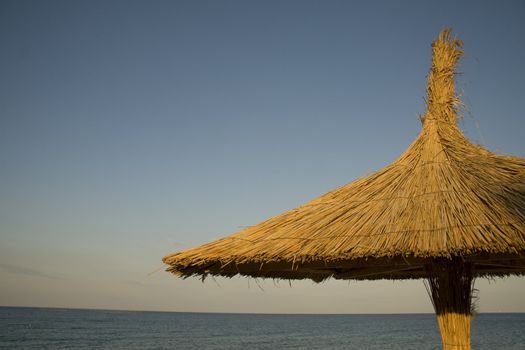 Close-up of wood and reed umbrella against blue sky and sealine