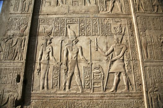 relief on a egyptian wall with a god a pharaoh an his wife