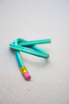 A green and blue striped rubber pencil tied in knot against gray background
