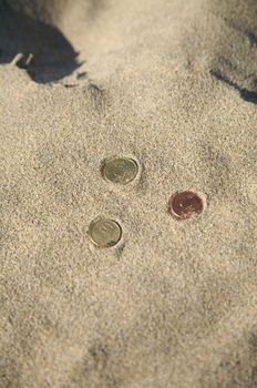 three euro coins at the sand of a beach