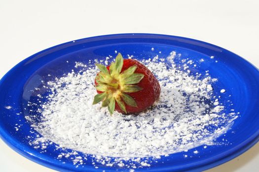 Single strawberry on blue plate with powdered sugar