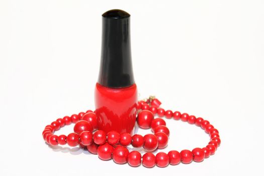 A bottle of red fingernail polish with strand of red wooden beaded necklace wrapped around