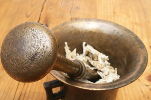 Antique mortar and pestle with white herbs on weathered wooden table