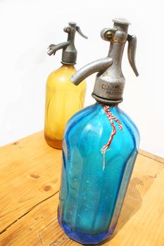Two antique seltzer bottles on weathered wooden table and white background