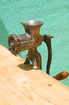 Antique meat grinder on weathered wooden table against turquoise wall