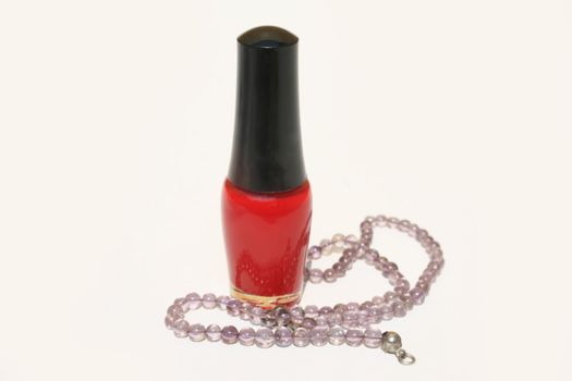 A bottle of red fingernail polish with purple beaded necklace 