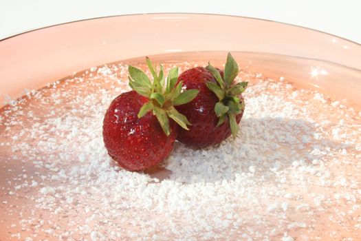 Two strawberries on powdered sugar on pink glass plate