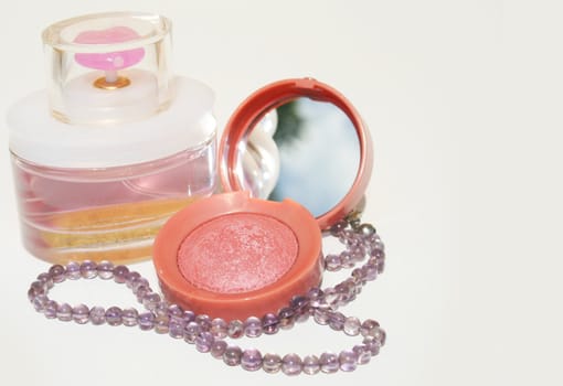 Perfume, blush and a purple beaded necklace on white background with copy space on right