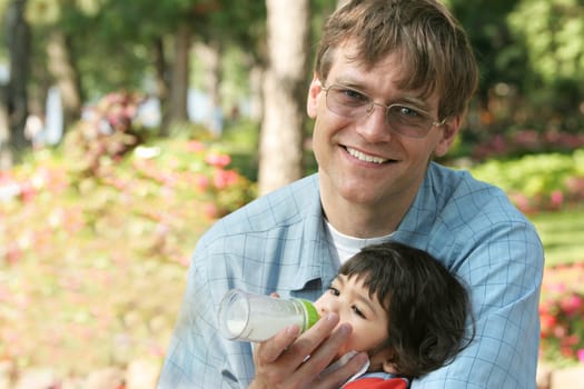 Father feeding baby a bottle in the park