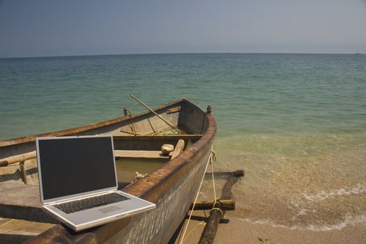 Laptop sitting on side of small fishing boat that is docked on beach