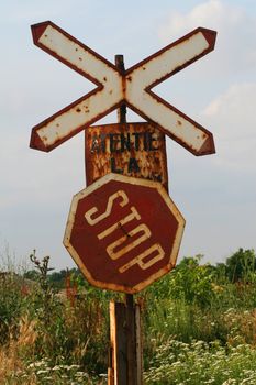 Rusty stop and train crossing signs on country road