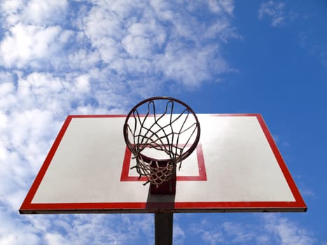 A basketball ring over a blue sky with clouds.