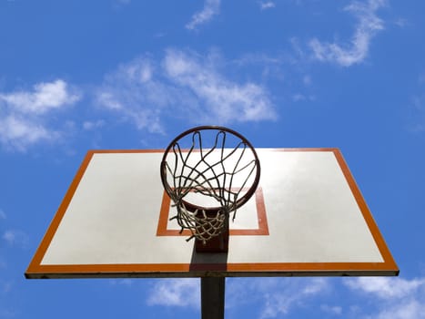 A basketball ring over a blue sky with clouds.