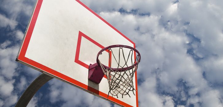 A basketball ring over a blue sky with clouds.