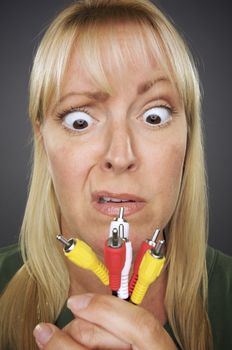 Confused Woman Holding Electronic Cables Against a Grey Background.