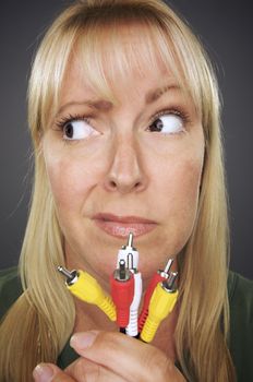 Confused Woman Holding Electronic Cables Against a Grey Background.