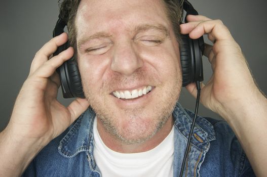 Man with Eyes Shut Wearing Headphones Enjoying His Music on a Grey Background.