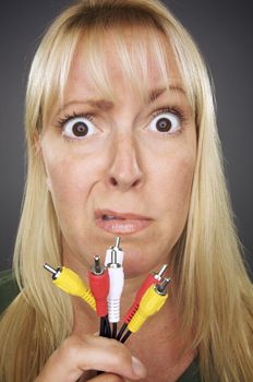 Confused Woman Holding Electronic Cables Against a Grey Background.