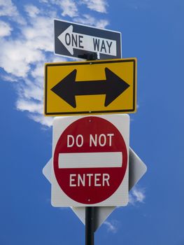 Three street signs over a blue sky with some clouds.