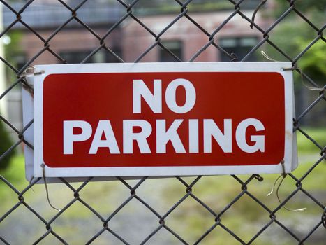 A No Parking sign hunging on a fence.