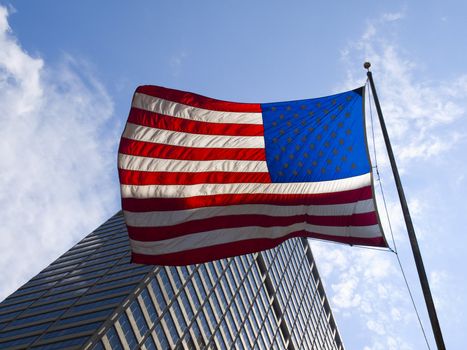 American flag waving against a skyscraper and a blue sky.