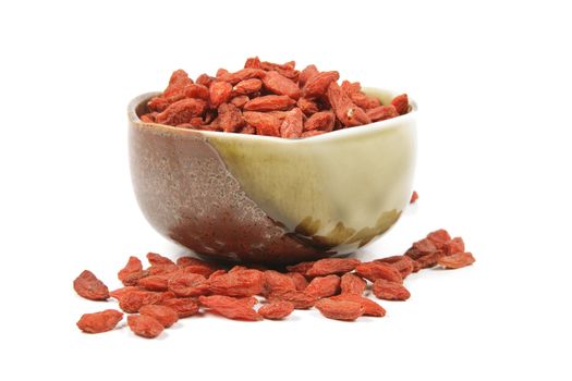 Red dry goji berries in a small green and brown dish on a reflective white background