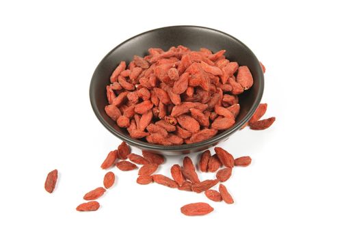 Red dry goji berries in a small black dish on a reflective white background