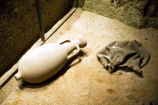 ancient jar and a bag on the floor sand of a cellar