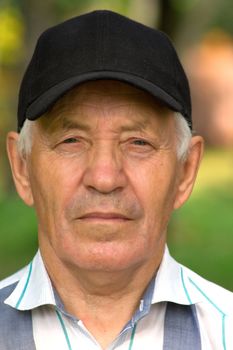 Portrait of the elderly man in a cap and a striped shirt against the nature