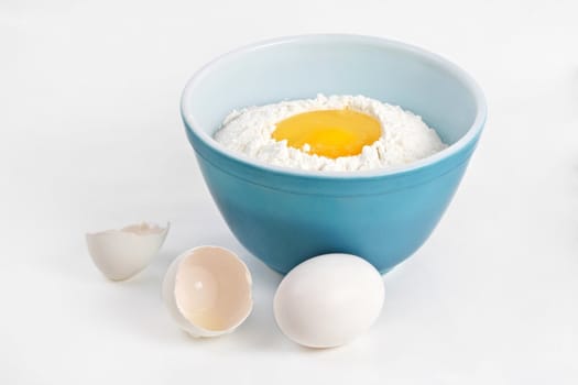 blue bowl filled with flour and broken eggs
