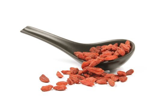Red dry goji berries on a black spoon with a reflective white background