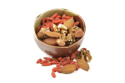 Red dry goji berries with mixed nuts in a green and brown bowl with on a reflective white background