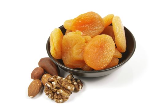 Dried juicy orange apricots with mixed nuts in a small black bowl on a reflective white background