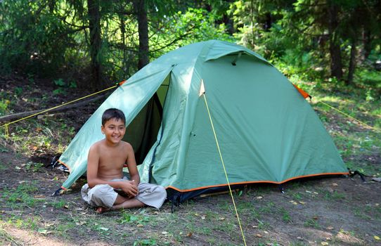 smiling boy near camping tent in forest