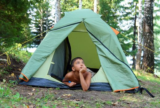 thoughtful boy in forest camping tent