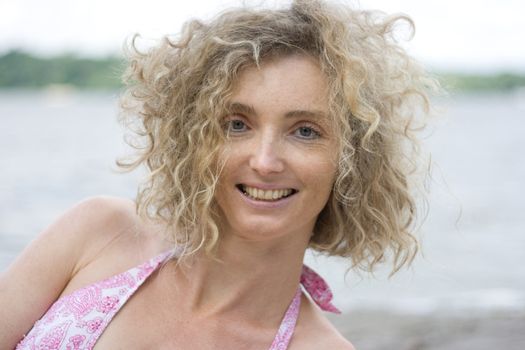 Portrait Of A Mature Blonde Woman With Curly Hair Near Water Side
