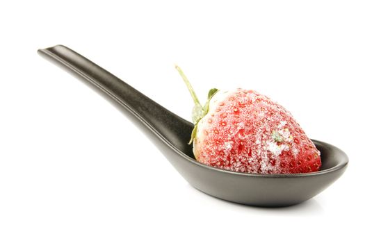 Red ripe frozen strawberry on a small black spoon with a reflective white background