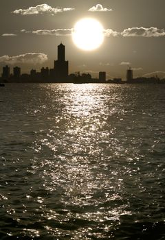 Harbor scenic with white sunset and black city silhouette of buildings near ocean in Kaohsiung, Taiwan.