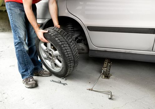 A male changing a tire on a car in a garage