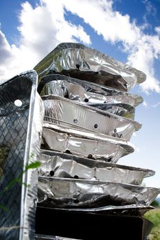 A stack of tinfoil disposable barbcues against a blue summer sky